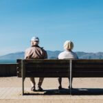 man and woman sitting on bench facing sea