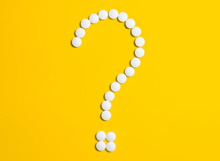 White pills arranged in a question mark shape on a bright yellow background, symbolizing medical queries.