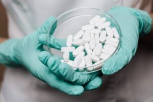 A healthcare professional in gloves holds a petri dish with white pills, demonstrating medical care.