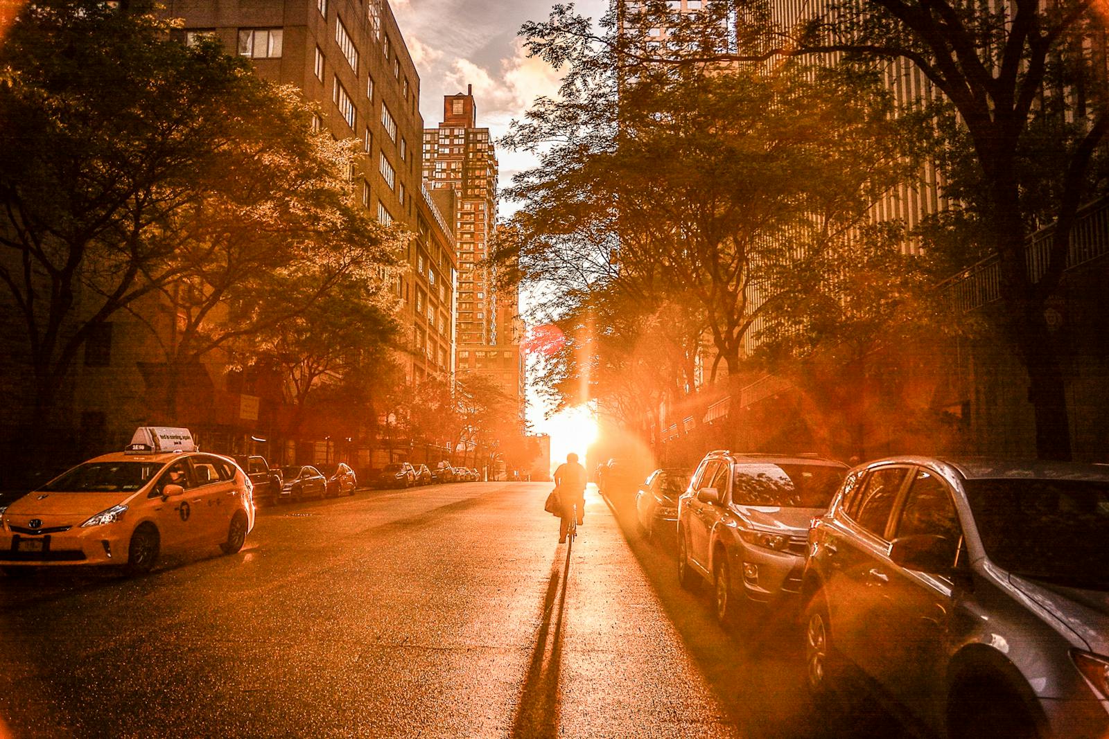 Silhouette of a cyclist during sunset on a New York City street with urban buildings and cars.