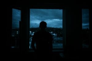 Man looks out a window at a night cityscape.