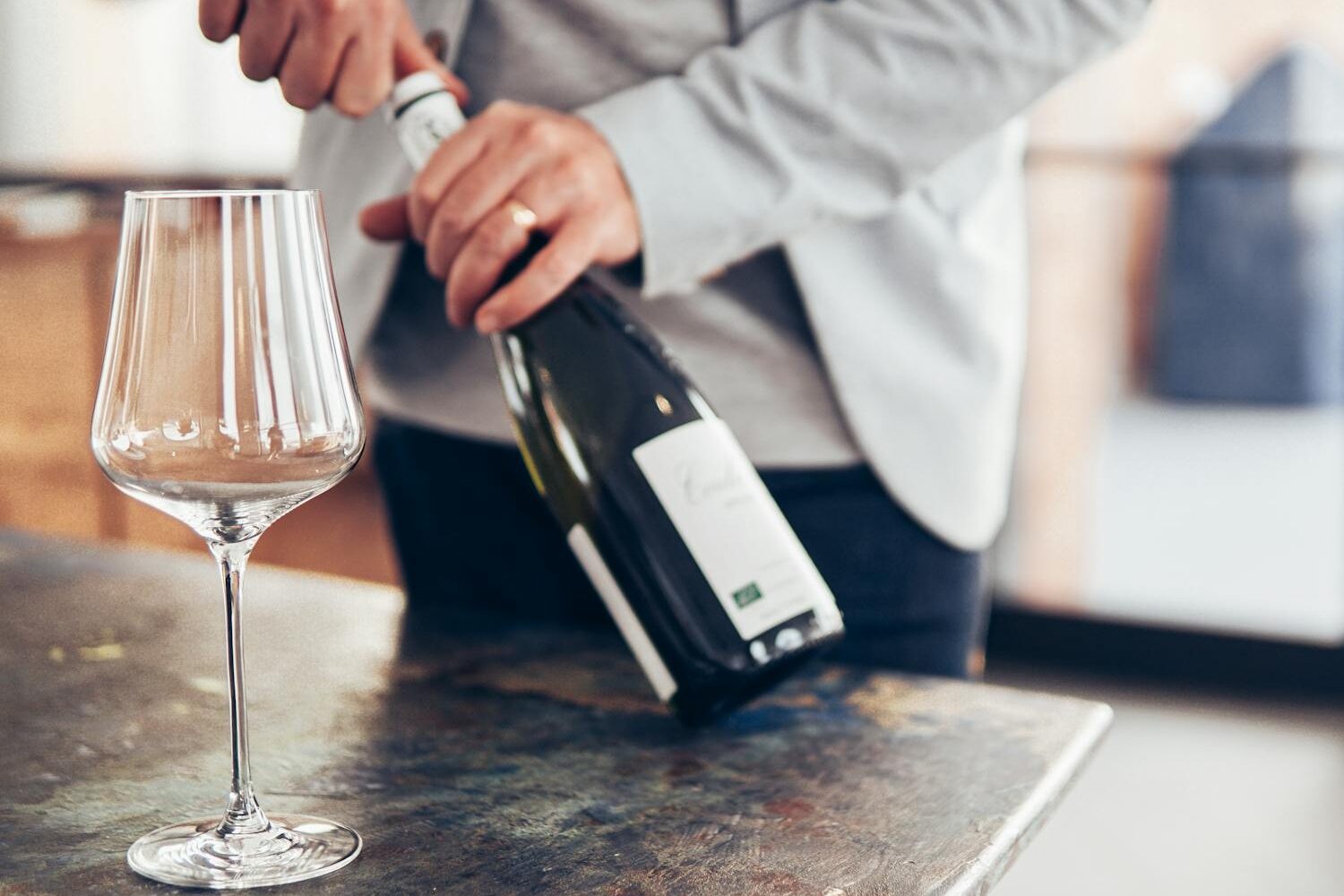 Close-up of a person elegantly opening a wine bottle beside an empty glass on a modern table.