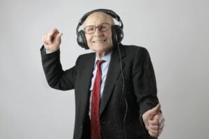 Happy senior man in formal attire delighting in music with headphones on a white background.