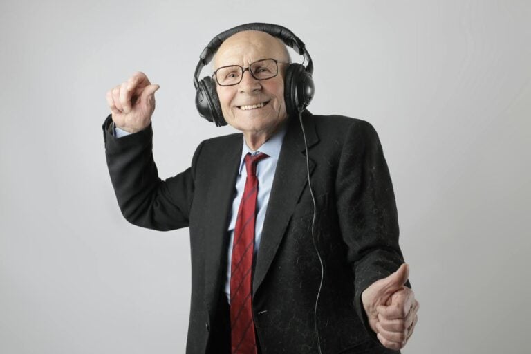 Happy senior man in formal attire delighting in music with headphones on a white background.