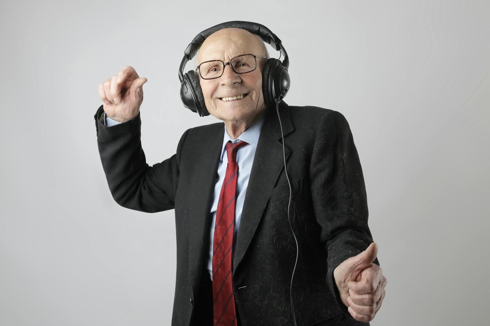 Happy senior man in formal attire delighting in music with headphones on a white background.