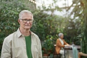 Elderly man with glasses in a lush greenhouse environment, focused and serene.