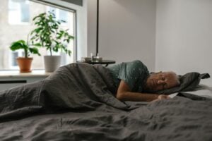 Senior man resting peacefully on a bed inside a room with natural light and plants.