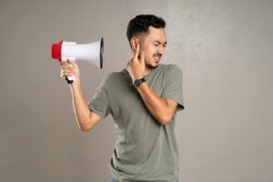 A man with a megaphone holding ear in discomfort, representing noise pollution or loud sounds.