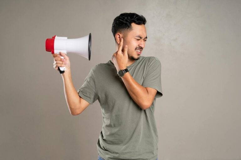 A man with a megaphone holding ear in discomfort, representing noise pollution or loud sounds.