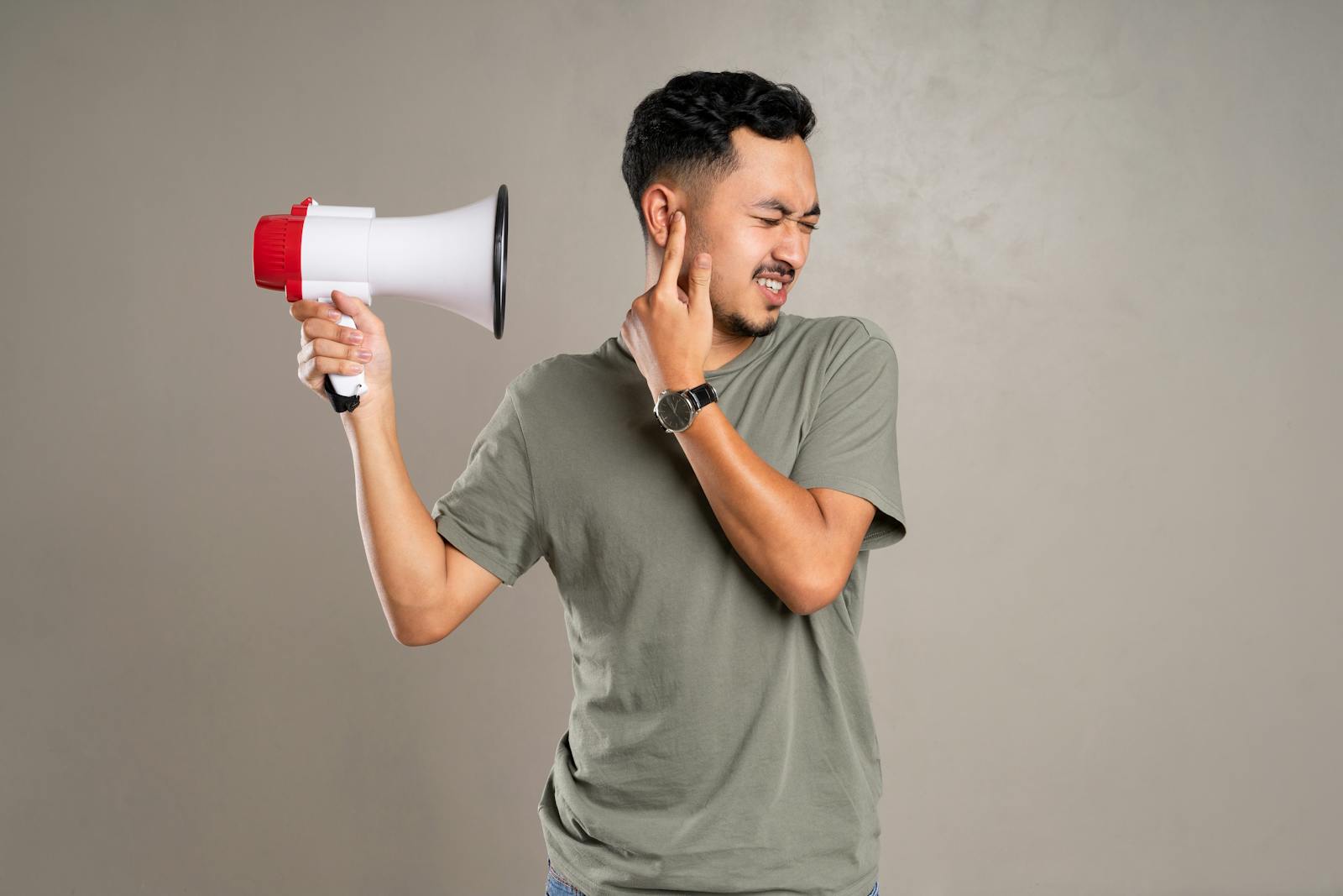 A man with a megaphone holding ear in discomfort, representing noise pollution or loud sounds.