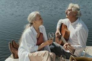 Elderly couple enjoying a romantic moment with guitar and wine by the lake.