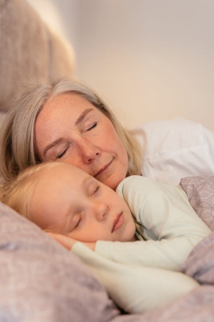 A serene moment as a grandmother and granddaughter cuddle and nap together indoors. (Photo by Mikhail Nilov on Pexels)