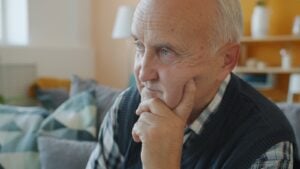 Elderly man with hand on chin, deep in thought.