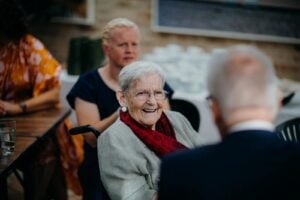 Smiling elderly woman enjoying company at an outdoor gathering, exhibiting warmth and happiness.