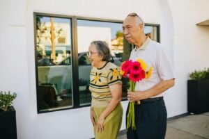 Happy senior couple walking outdoors, holding colorful flowers. A delightful moment capturing love and togetherness.